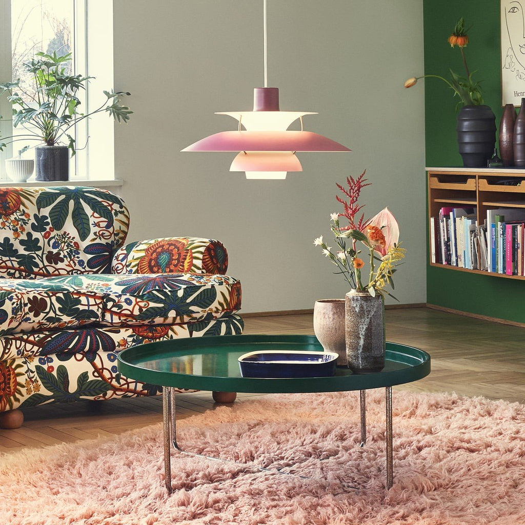 Suspension scandinave en métal coloré rose suspendue au-dessus d'une table basse dans un salon vert