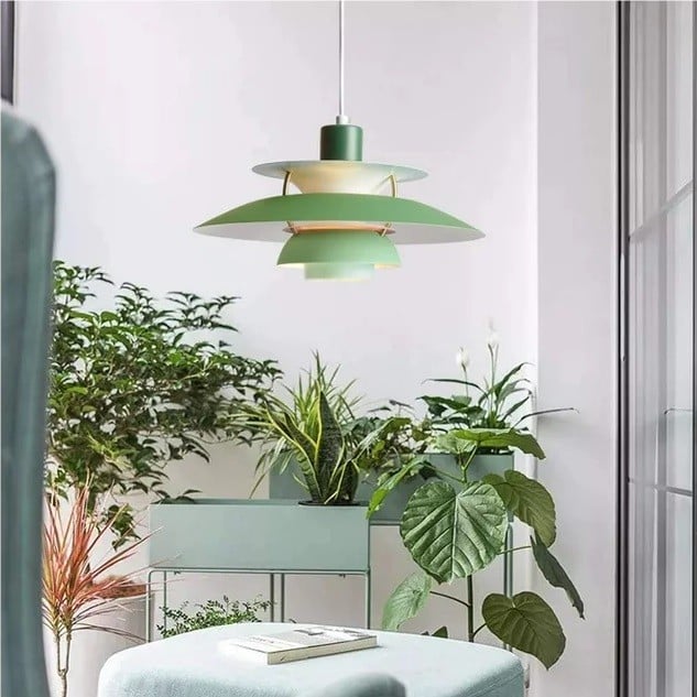 Suspension scandinave en métal coloré verte devant une baie vitrée entourée de plantes
