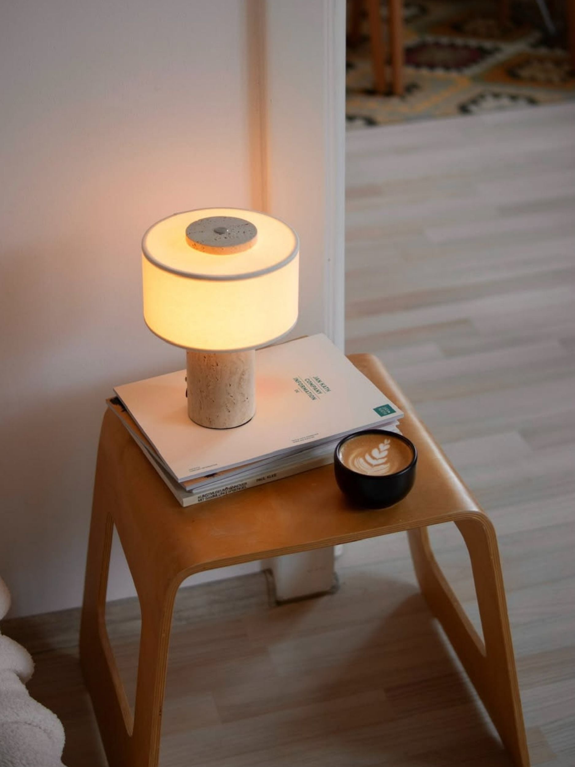 Lampe de table sans fil en travertin posée sur un tabouret en bois