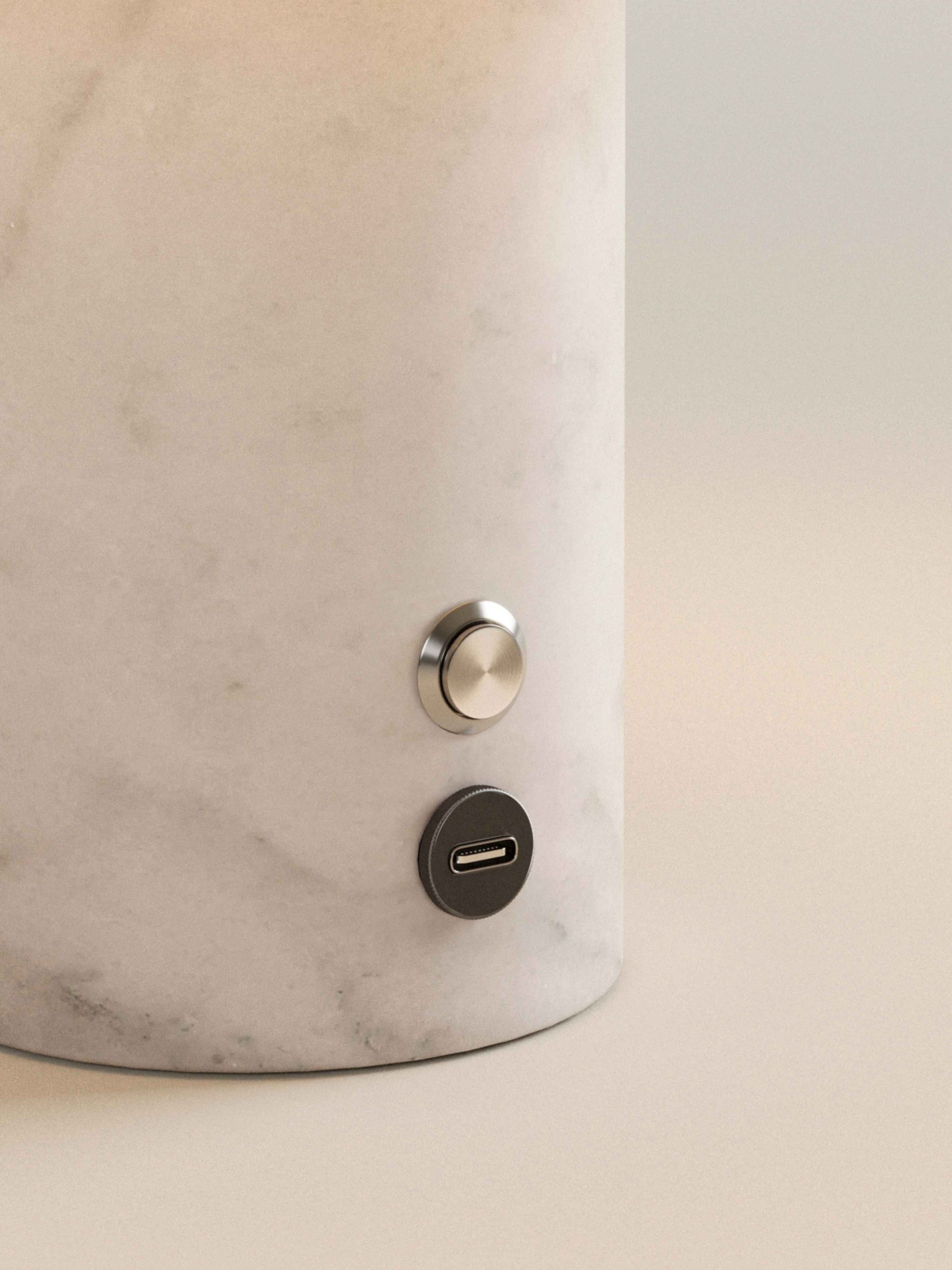 Gros plan sur le socle en marbre blanc, son bouton et son port USB-C