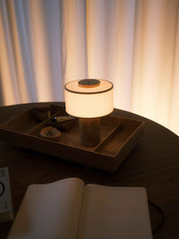 Lampe de table sans fil en travertin allumée sur une table en noyer