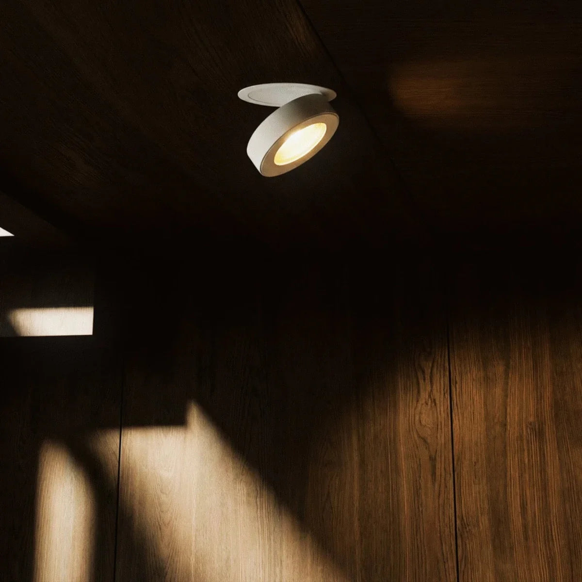 Spot encastrable orientable blanc éclairant un mur en bois sombre