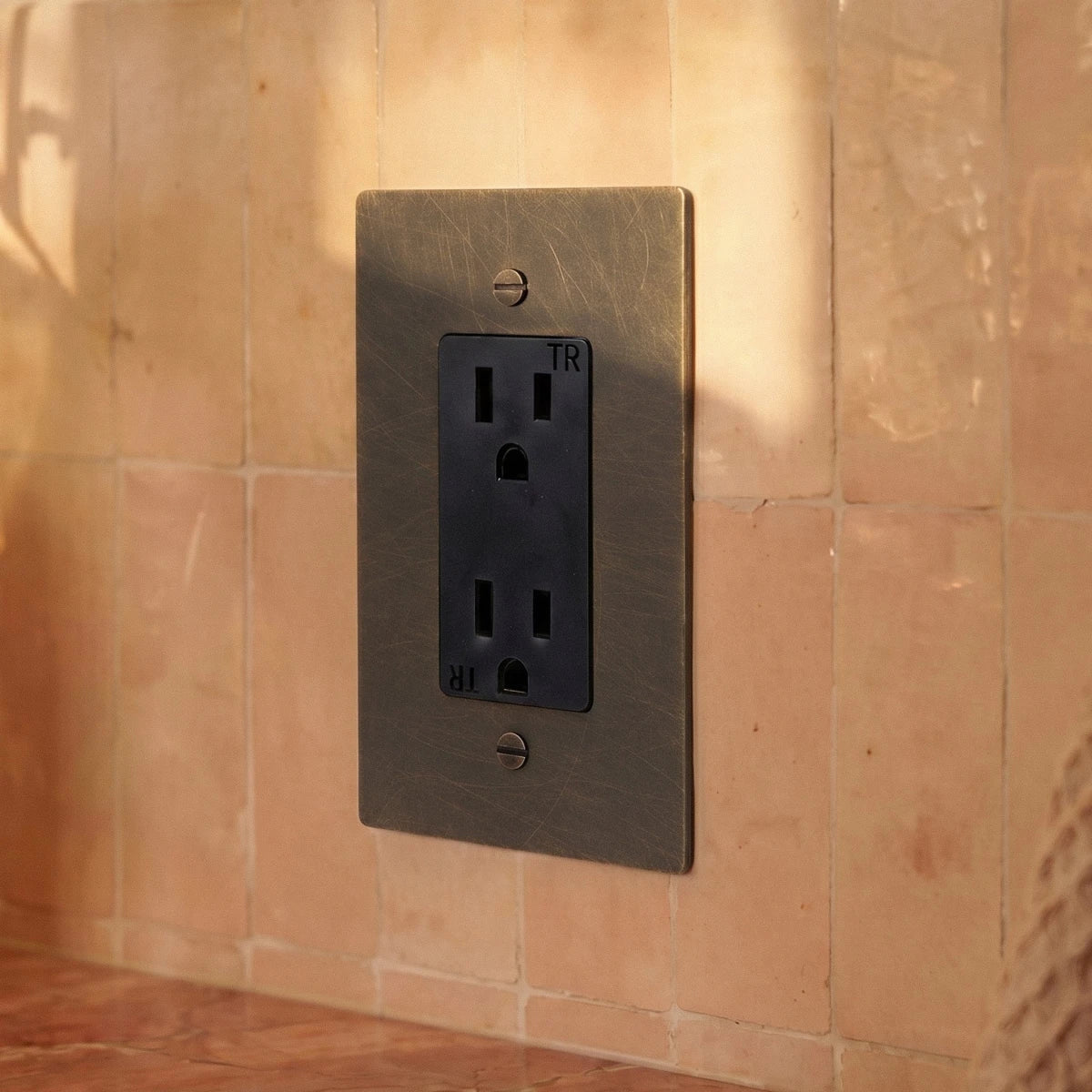 Gros plan sur une prise électrique noire sur un mur rosé en lumière rasante