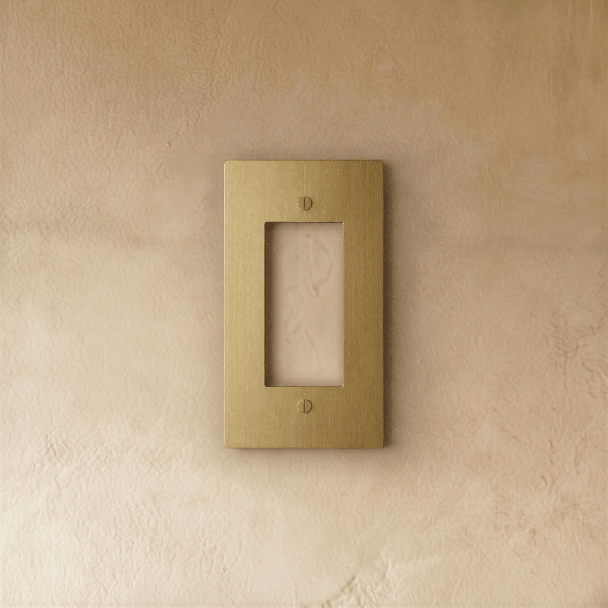 Plaque interrupteur en laiton 1 poste fixée sur un mur beige