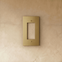 Plaque interrupteur en laiton 1 poste fixée sur un mur beige