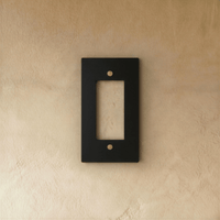 Plaque interrupteur noir et laiton 1 poste fixée sur un mur beige