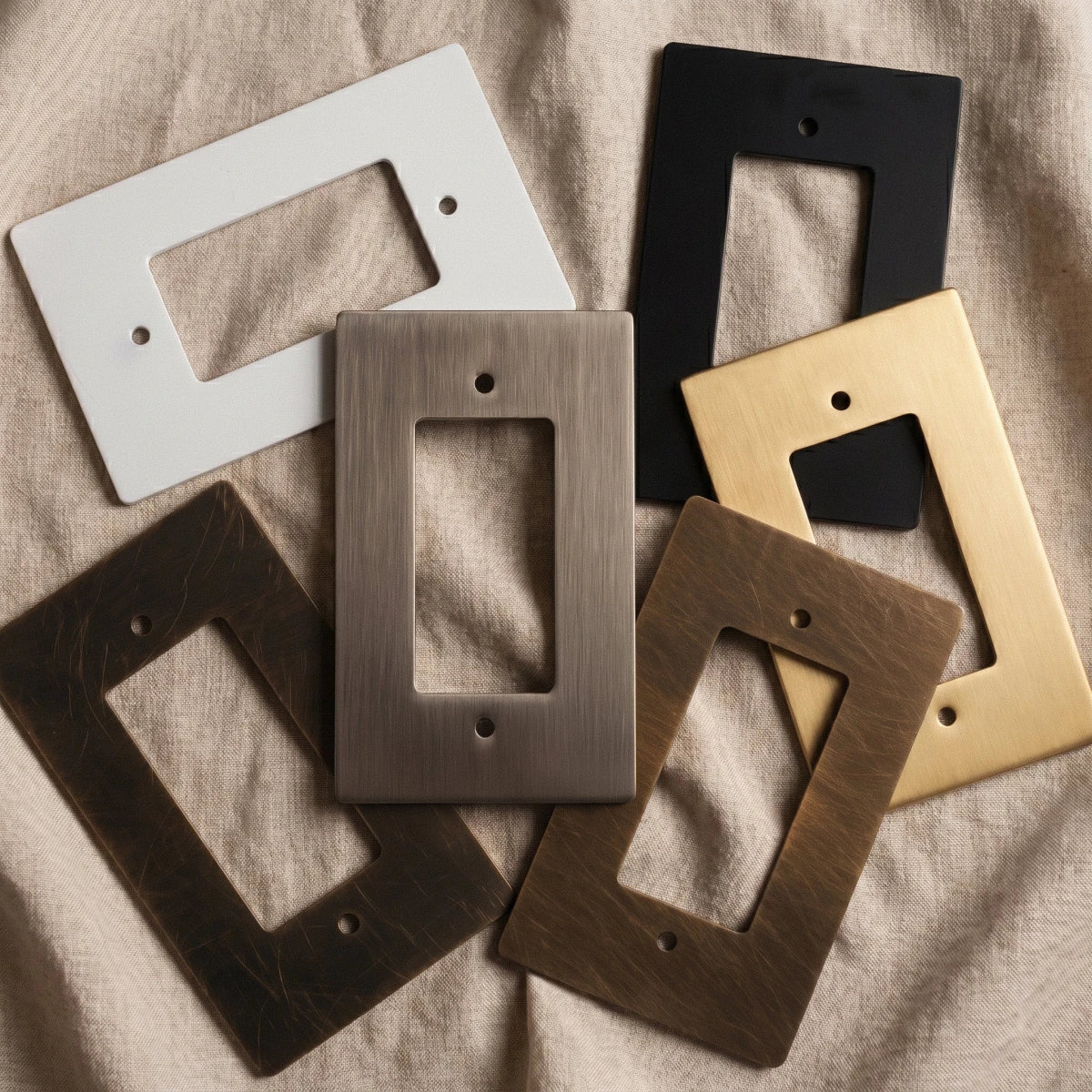 Plaques interrupteur en finitions blanc, noir et laiton posées sur un tissu